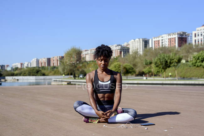 Une Afro-Américaine au sommet d'une salle de sport et des jambières assises dans un lotus posent et étirent les mains tout en relaxant — Photo de stock