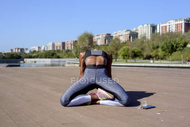 Афроамериканка в спортивном топе и ногах, сидя и растягиваясь, расслабляясь после тяжелой тренировки в городском парке — стоковое фото