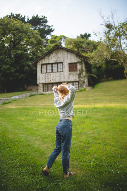 Back view of casual calm young woman enjoying stroll on green meadow near wooden house in rural village in Asturias, Spain — Stock Photo