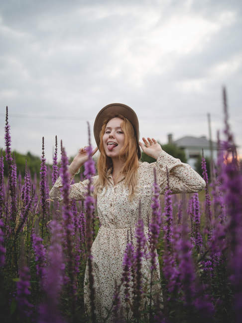 Woman in trendy hat looking at camera while enjoying smell of salvia blossom in meadow of Asturias, Spain — Stock Photo