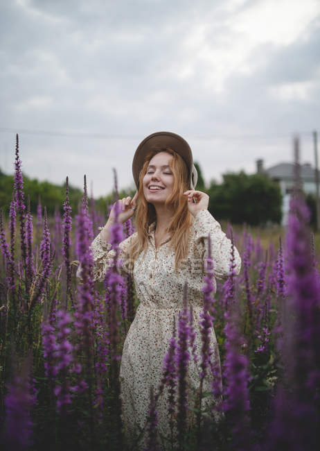 Woman in trendy hat with closed eyes enjoying smell of salvia blossom in meadow of Asturias, Spain — Stock Photo