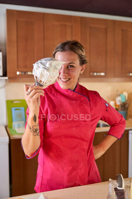 Счастливая уверенная женщина-повар демонстрирует венчик с белым вкусным взбитым сливочным кремом — стоковое фото
