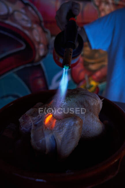 Poulet frais entier pendant le traitement avec lance-flammes au gaz brillant dans la cuisine du restaurant — Photo de stock