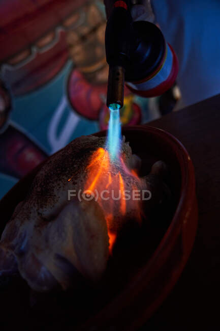 Целый свежий цыпленок во время обработки с огнемётом с ярким газом в кухне ресторана — стоковое фото