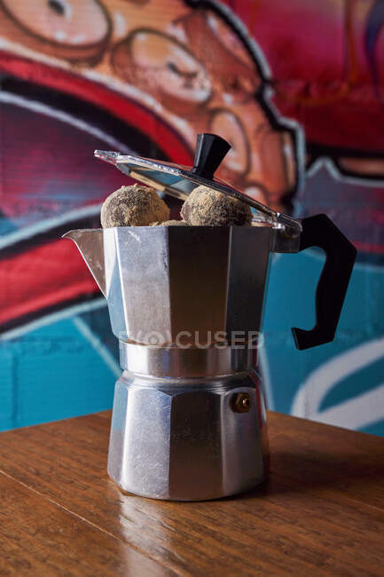 Dall'alto della caffettiera in acciaio inox con palline rotonde di deliziosi tartufi di cioccolato serviti su tavolo contro parete su graffiti — Foto stock