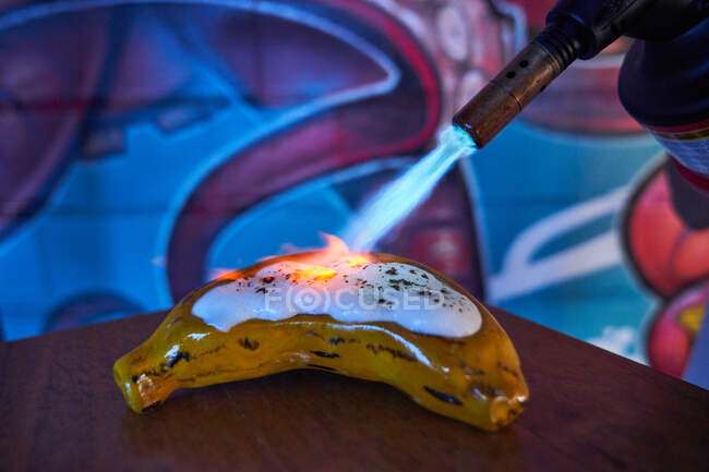 Faceless chef using gas torch and grilling shiny white meringue on banana shaped pastry in restaurant — Stock Photo