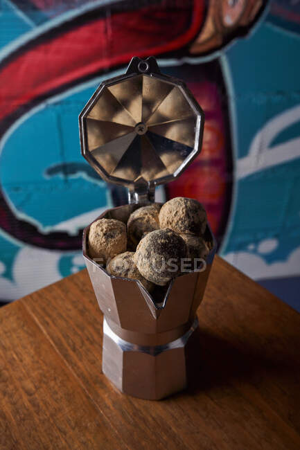 Dall'alto della caffettiera in acciaio inox con palline rotonde di deliziosi tartufi di cioccolato serviti su tavolo contro parete su graffiti — Foto stock