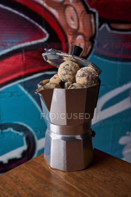 Сверху из нержавеющей плиты кофеварка с круглыми шариками вкусных шоколадных трюфелей подается на столе к стене на граффити — стоковое фото