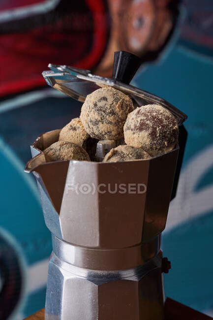 Desde arriba de la estufa de café inoxidable con bolas redondas de deliciosas trufas de chocolate servidas en la mesa contra la pared en graffiti - foto de stock