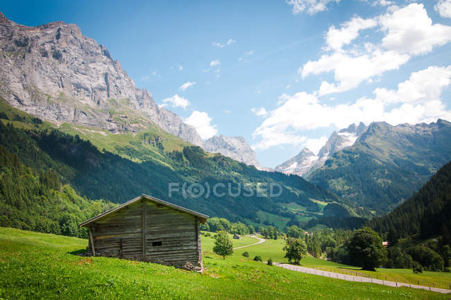 Vista panorâmica da manhã da cabana abandonada no prado verde com estrada que leva aos Alpes na Suíça — Fotografia de Stock