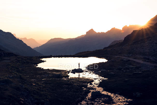 Силуэт человека, балансирующего на берегу и отражающегося в спокойной воде, окруженной горами в Швейцарии — стоковое фото