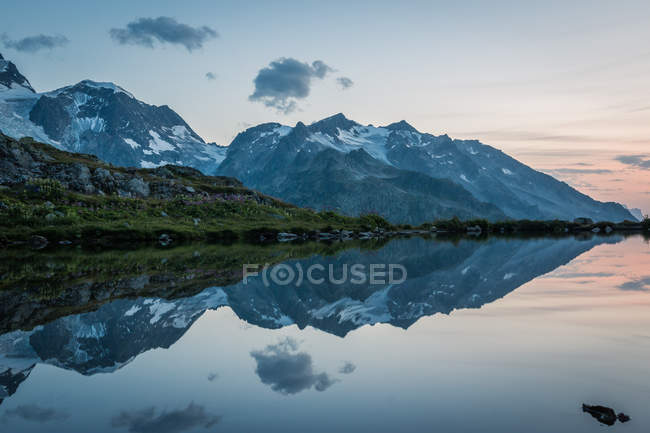 Empty coast of calm lake in snowy mountains reflecting sky in Switzerland — Stock Photo