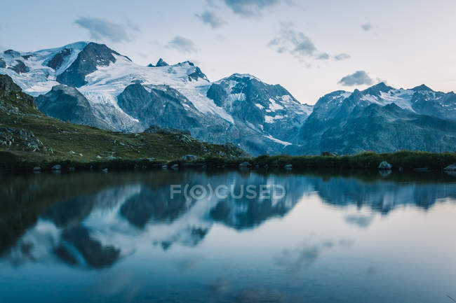 Empty coast of calm lake in snowy mountains reflecting sky in Switzerland — Stock Photo