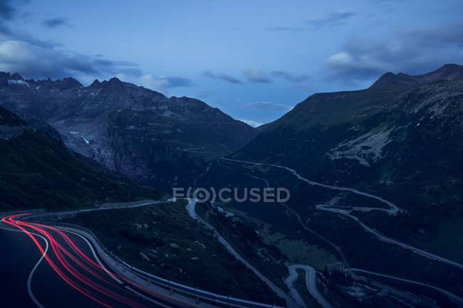 Вечерний пейзаж змеиной дороги с красными огнями автомобилей с изгибом в горах Швейцарии — стоковое фото