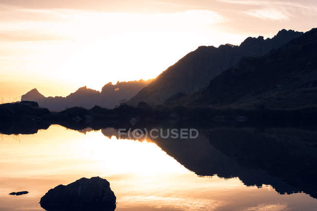 Breathtaking landscape of motionless water reflecting sky in warm sunset light and mountains in Switzerland — Stock Photo