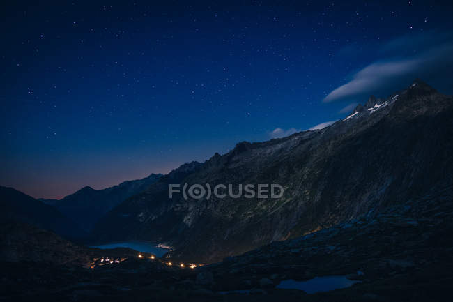 Mountain range and river between slopes with lights above in Switzerland — Stock Photo