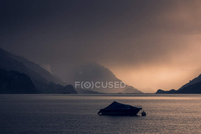 Paisaje tranquilo de barco oscuro en agua ondulada bajo el cielo nublado gris en las montañas de Suiza - foto de stock