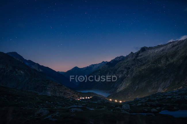 Catena montuosa e fiume tra i pendii con luci in Svizzera — Foto stock