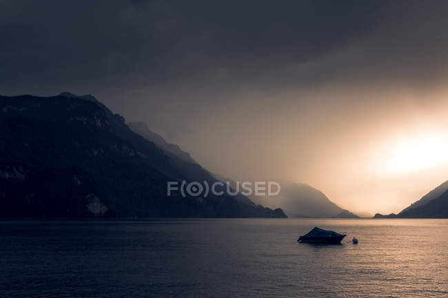Спокійний пейзаж темного човна у хвилястій воді під сірим хмарним небом у горах Швейцарії. — стокове фото