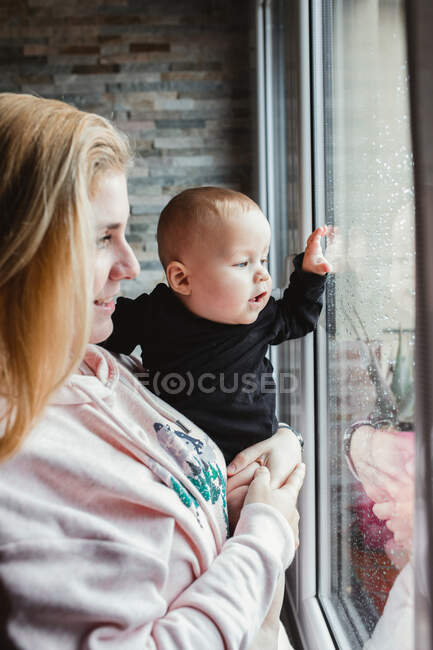 Madre y bebé mirando por la ventana - foto de stock