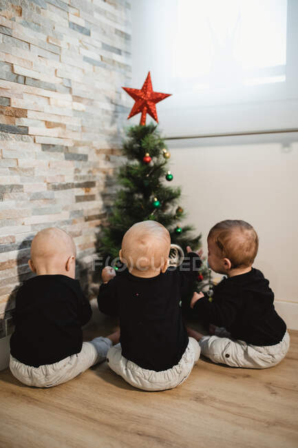 Bebés anónimos cerca del árbol de Navidad - foto de stock