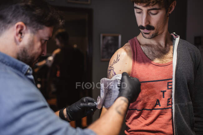 Maître de tatouage enlever le modèle sur l'avant-bras du client — Photo de stock