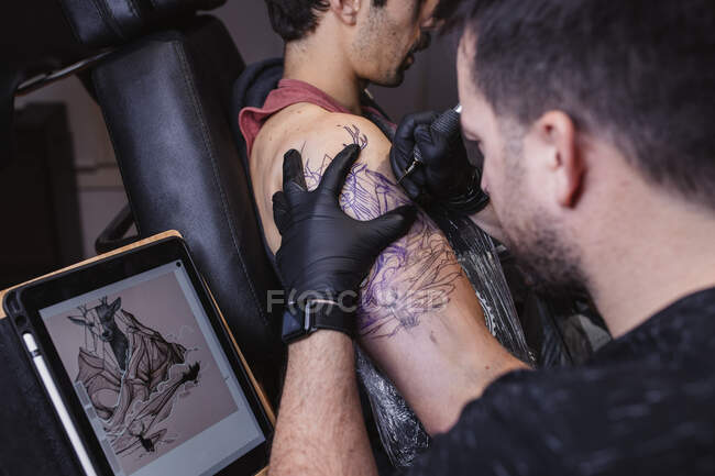 Maître faisant le tatouage sur l'avant-bras du client masculin — Photo de stock