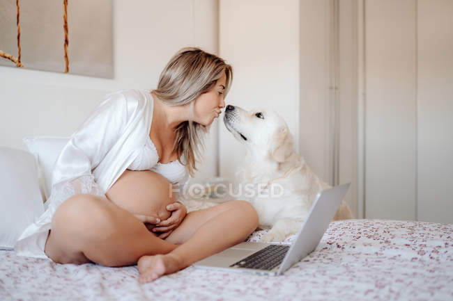 Smiling blonde pregnant female kissing labrador dog standing beside and looking at camera — Stock Photo