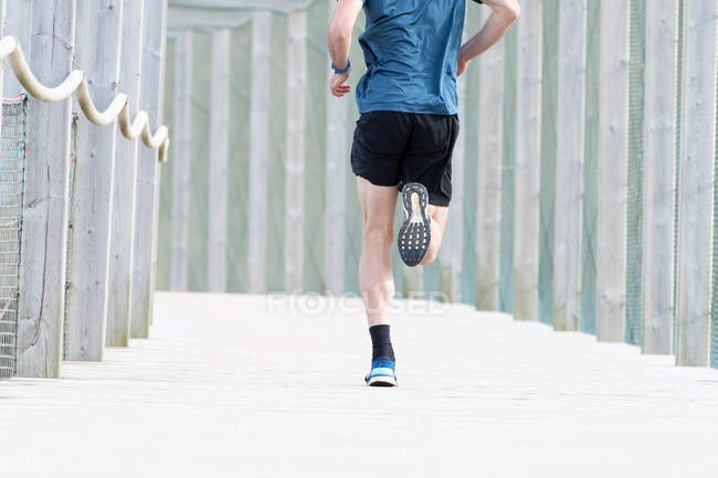Cropped image of male athlete in blue t shirt and shorts running outdoors under cover — Stock Photo