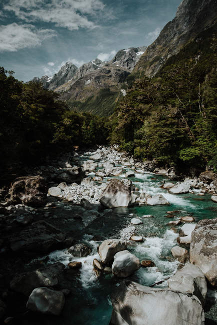 Bellissimo paesaggio neozelandese con stretto fiume di montagna tra rocce e verdi colline nelle soleggiate giornate estive con nuvole sul cielo — Foto stock
