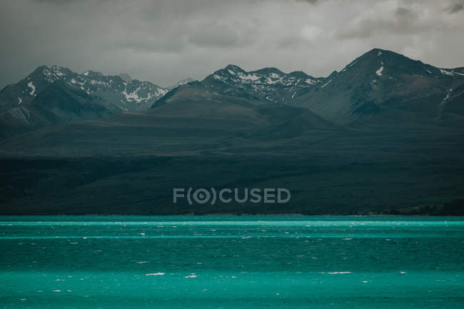 Amazing New Zealand landscape with turquoise sea water and rocky mountains with snow on tops against cloudy sky — Stock Photo