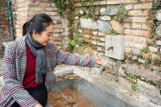 Jeune femme en vêtements décontractés se laver les mains dans la fontaine de rue — Photo de stock