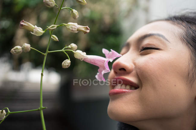 Charming Asian female on vacation sniffing flower at city street — Stock Photo