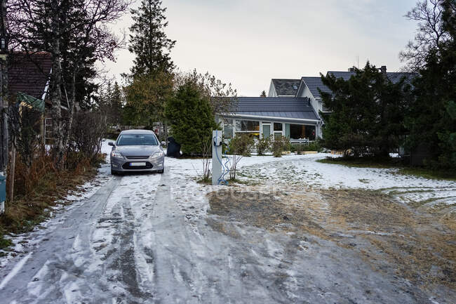 Сірий електричний автомобіль на засніженому подвір'ї біля заміського будинку серед красивого саду взимку — стокове фото