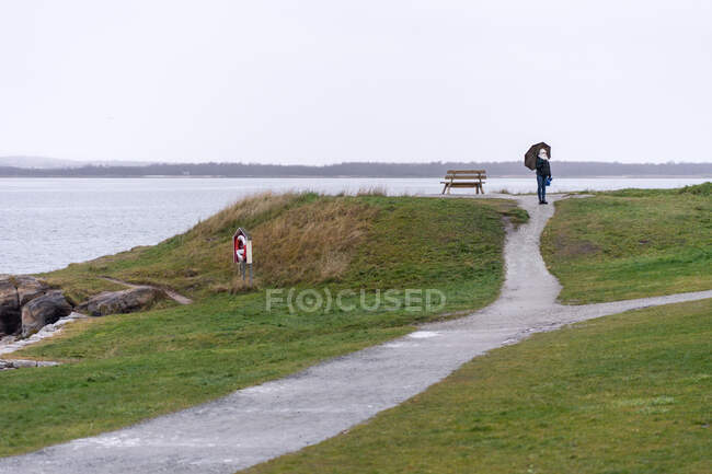 Viajante com guarda-chuva andando na costa elevada — Fotografia de Stock