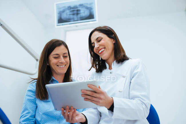 Стоматолог разговаривает с клиентом, показывая документ с информацией — стоковое фото