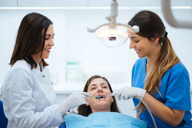 Dentista e assistente examinando a boca do paciente em cadeira com ferramentas — Fotografia de Stock