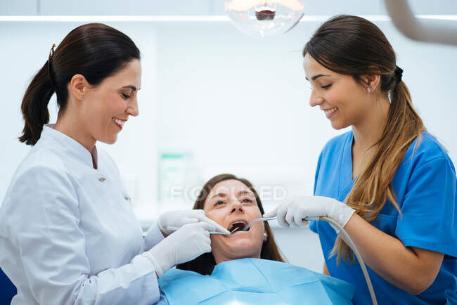 Стоматолог и ассистент осматривает рот пациента в кресле с t — стоковое фото