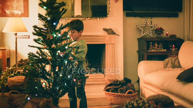 Мальчик украшает елку вечером — стоковое фото