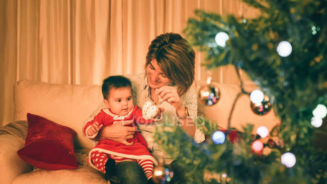 Madre jugando con el bebé cerca del árbol de Navidad - foto de stock