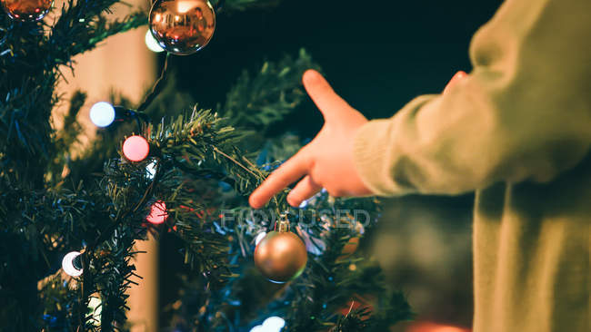 Zugeschnittenes Bild eines Jungen, der abends den Weihnachtsbaum schmückt — Stockfoto
