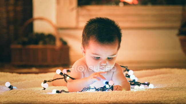 Bebê brincando com guirlanda leve no dia de Natal — Fotografia de Stock