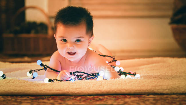 Baby spielt am ersten Weihnachtstag mit Lichterkette — Stockfoto