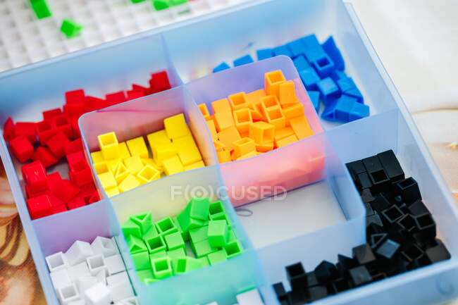Organizador de caja transparente azul con pequeñas piezas de mosaico de plástico de colores para niños juego de mesa educativo con sección vacía - foto de stock