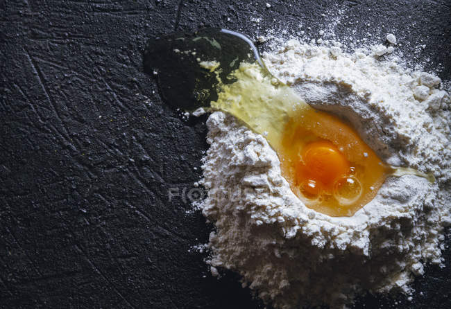 Vista superior do ovo quebrado na farinha na superfície preta texturizada — Fotografia de Stock