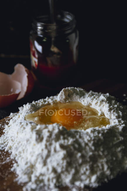 Broken egg in flour on textured black surface with glass pot — Stock Photo