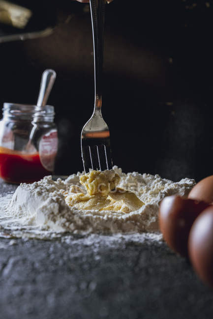 Вилка смешивания яйца и муки во время приготовления теста для макарон на черном столе — стоковое фото
