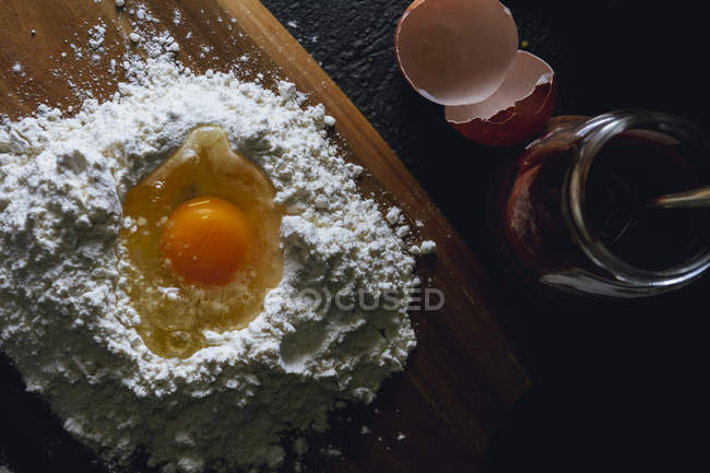 Верхний вид разбитого яйца в муке на текстурированной черной поверхности со стеклянным горшком — стоковое фото