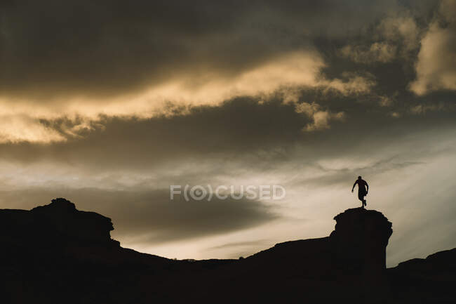 From below of male silhouette in motion on mountain with beautiful cloudy sky on background — Stock Photo