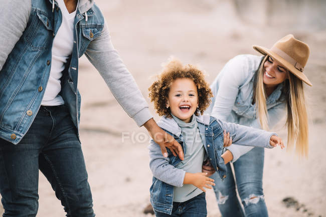 Feliz multirracial padres jugando con sonriente adorable rizado étnico niño en arenoso desierto - foto de stock